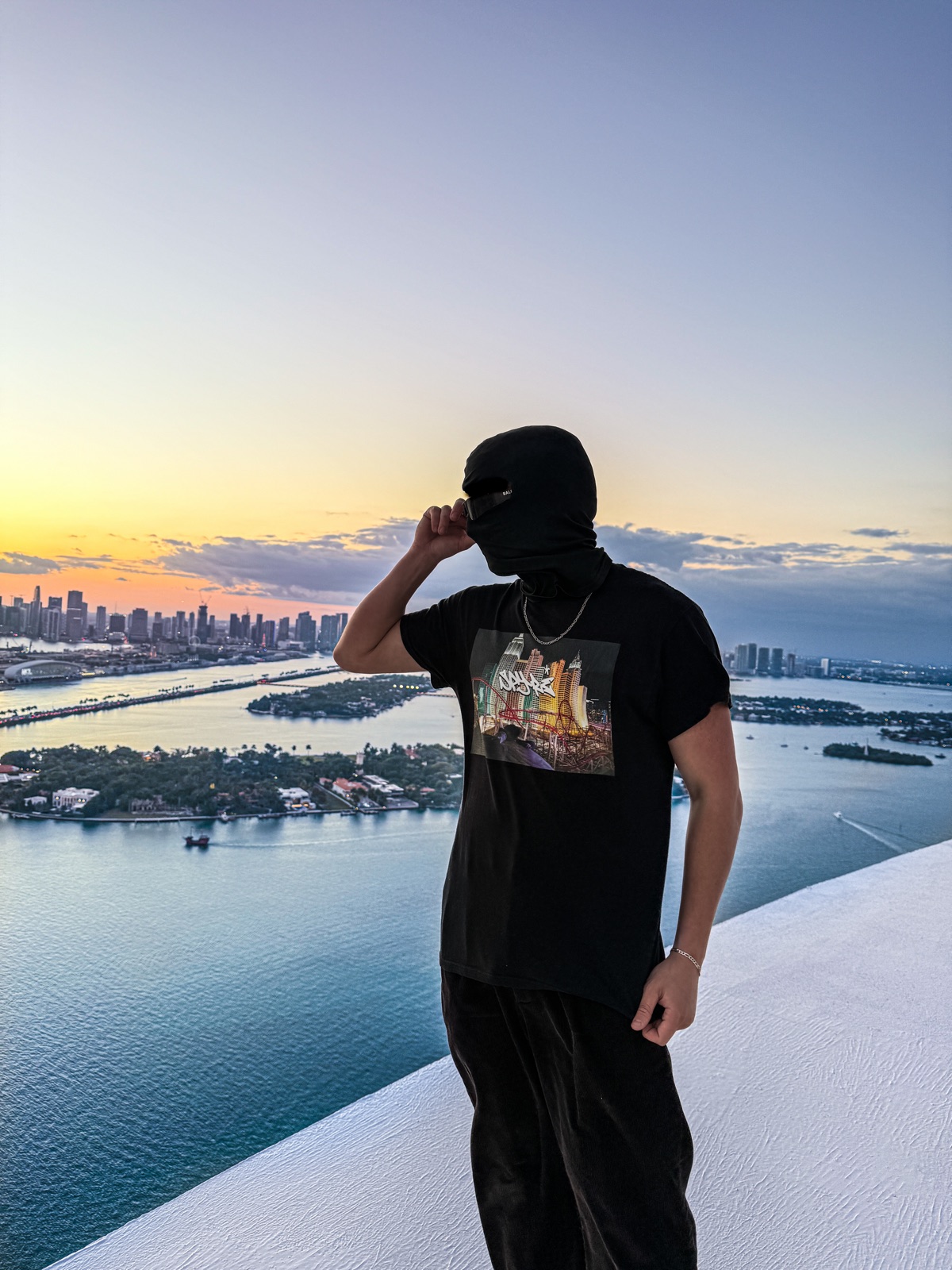 A masked Spyre wearer on a rooftop ledge above Miami at sunset